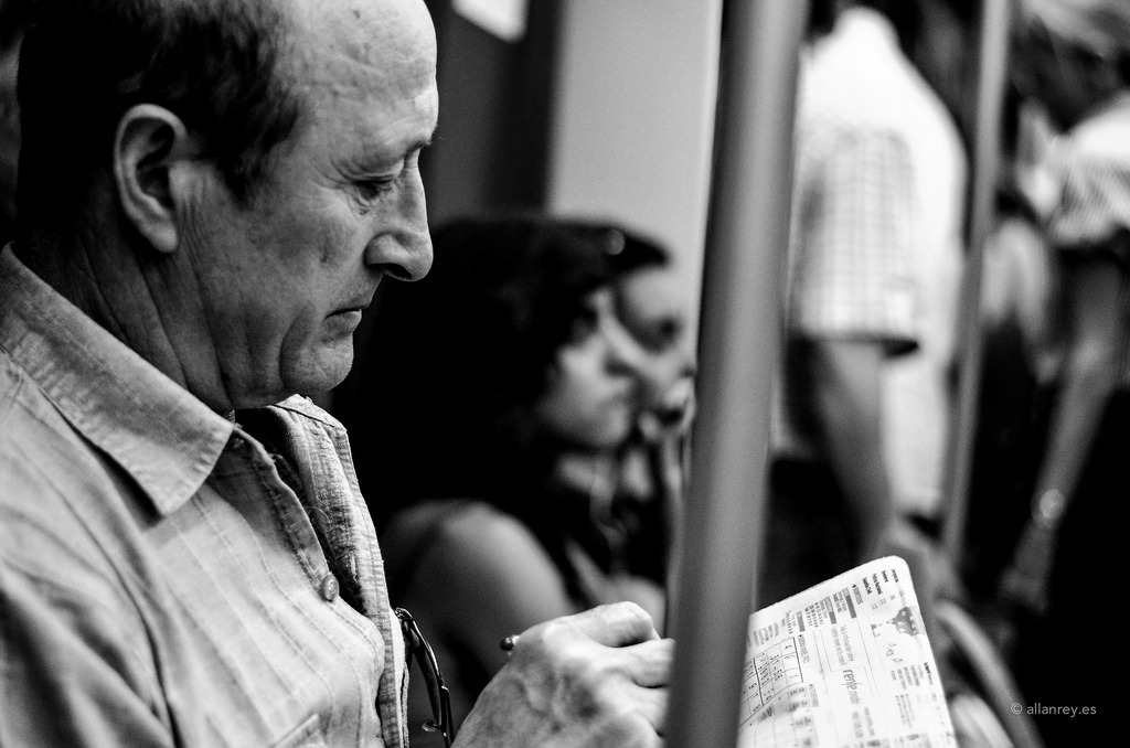 A photograph of a man seated in a Metro train solving a Suduko puzzle on a newspaper.
